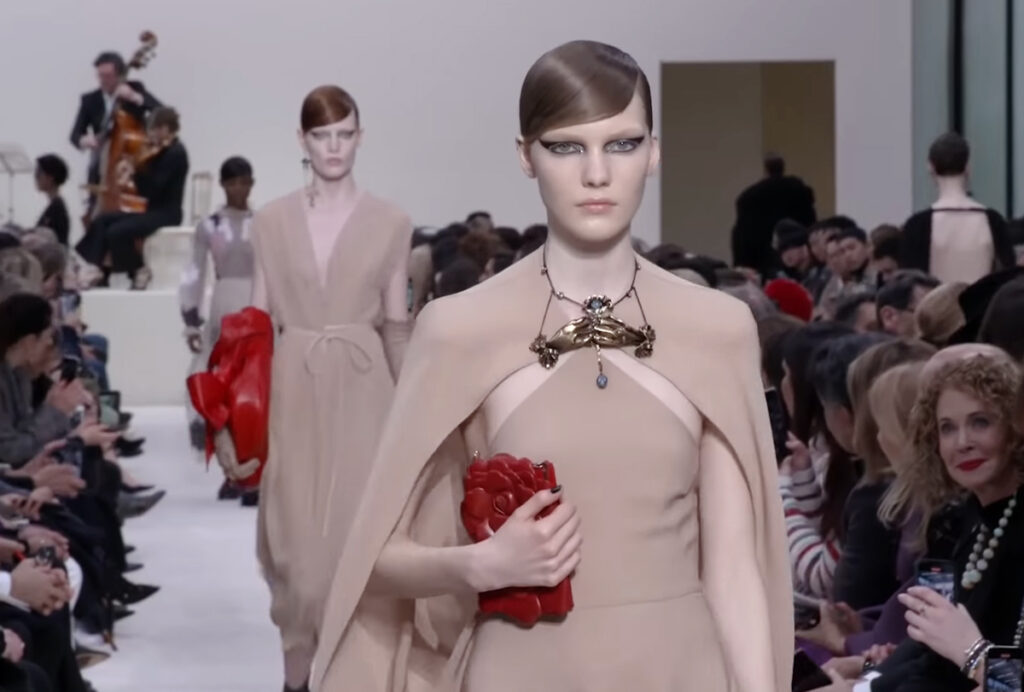 Biege dress with a biege cape, heavy formal jewelry and a red handbag with floral motifs close-up photo. A Symphony of Fashion with The Fall Winter 2020 Collection by Valentino